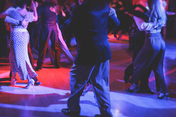 Couples dancing traditional latin argentinian dance milonga in the ballroom on a festival, tango studio, salsa, bachata and kizomba lesson in the red and purple lights, rehearsal in the dance class - obrazy, fototapety, plakaty