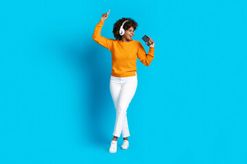 Fototapeta na wymiar Happy black woman using headphones and cell phone, singing karaoke