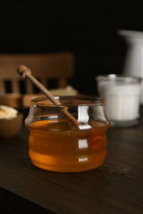 Jar with honey, milk, bread and butter on wooden table