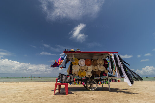 tent selling hats, sarongs and sunglasses on the beach in S&atilde;o Miguel dos Milagres. Green water and blue sky on the beach. Winds on sarongs