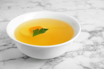 Delicious bouillon with egg and parsley in bowl on white marble table