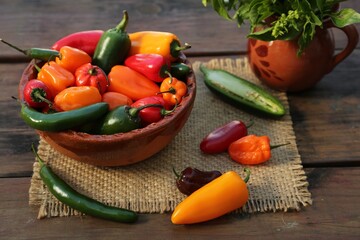 Many different ripe chili peppers on wooden table