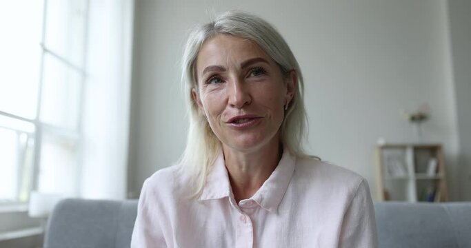 Pretty middle-aged woman sits on couch staring at camera having conversation, talking to friend, enjoy pleasant communication to family living abroad use video call application. Virtual meeting event
