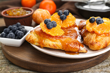 Fresh tasty puff pastry with sugar powder, jam, tangerines and blueberries on wooden table, closeup