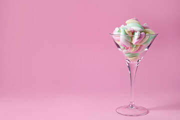 Beautiful martini glass with colorful marshmallows on pink background. Space for text