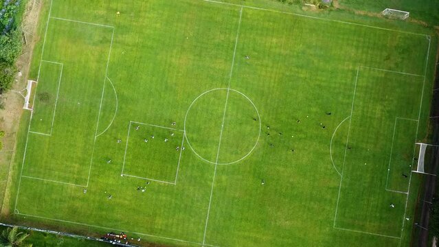 Vuelo de drone, sobre cancha de futbol con jugadores entrenando a pleno sol, al fondo un campo de agave.