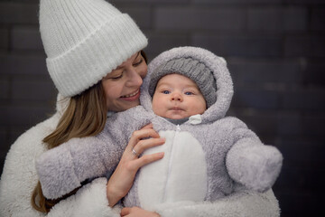 young woman with a baby in her arms walking around the city. mom and son are walking in cold weather, dressed in trendy warm clothes. Mom gently hugs her child.
