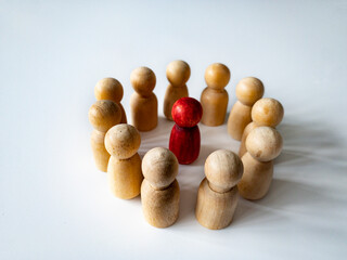 Red wooden doll figure surrounded by other doll figure on white background. Harassment and bully...