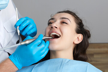 Dentist drilling tooth of female patient in dental chair