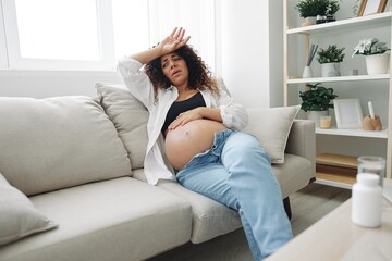 Fototapeta premium Pregnant woman headache lies at home on the couch fatigue and heaviness in the last month of pregnancy before childbirth, motherhood difficulties