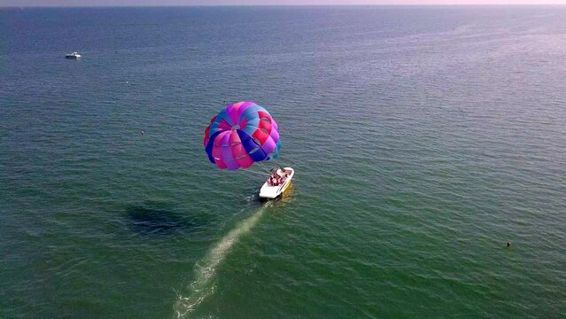 aerial drone shot of boat pulling parachute over the sea in lignano parasailing