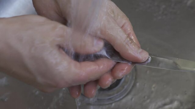 man's hands washing a metal knife in a metal sink