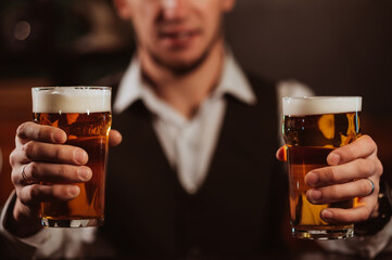 happy bartender serves two glasses of light draft beer lager with foam in hand at bar in pub