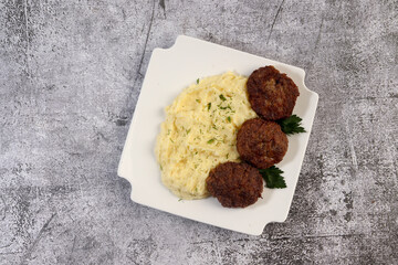 Mashed potatoes with cutlets and herbs on a white square  plate on a dark background. Top view, flat lay