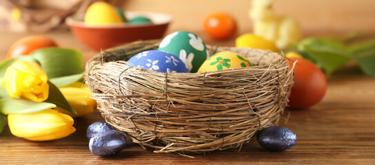 Nest with painted Easter eggs and candies on wooden table
