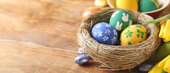 Nest with painted Easter eggs and candies on wooden background with space for text
