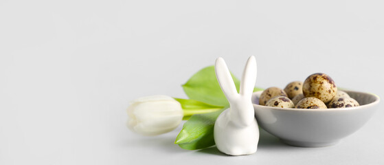 Bowl with Easter eggs, bunny and tulip flower on light background with space for text