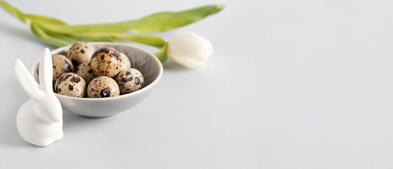 Bowl with Easter eggs, bunny and tulip flower on light background with space for text