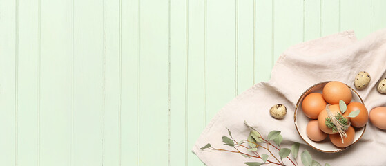 Bowl with Easter eggs and eucalyptus branch on green wooden background with space for text