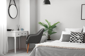 Interior of modern bedroom with table, mirror and houseplant