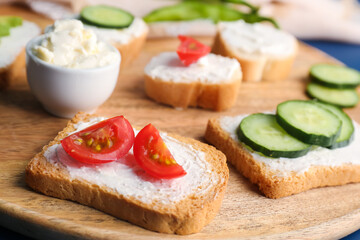 Fototapeta na wymiar Wooden board of tasty sandwiches with cream cheese and vegetables, closeup