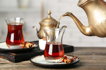 Pouring of hot Turkish tea from teapot into glass on wooden table