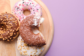 Wooden board with delicious donuts on lilac background