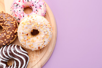 Wooden board with delicious donuts on lilac background, closeup