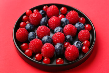 Plate of fresh berries on red background
