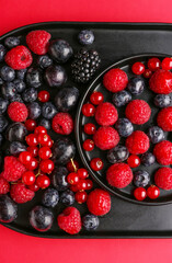 Plates of fresh berries on red background, closeup