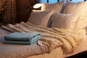 Folded electric heating pad with controller on bed in dark room, closeup