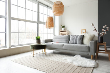 Cozy interior of living room with grey sofa, pouf and fur carpet near window