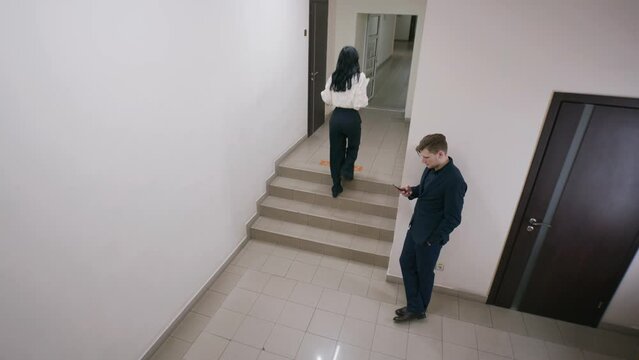 Successful man in suit stands at lobby, chats with client or surfs internet by phone. Business people walking corridor between work process at office with modern design. Security camera and CCTV.