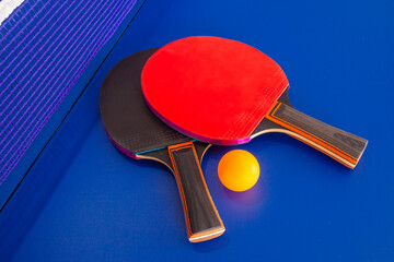 Two table tennis or ping pong rackets and balls on a blue table with net; shallow DOF, selective focus 