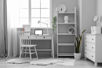 Interior of light office with workplace, shelving unit and houseplants