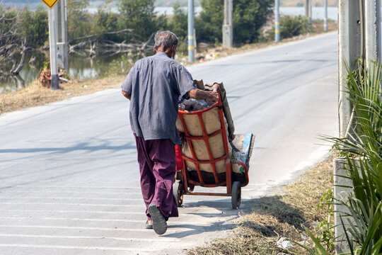 A old man pushing a trolley with a load of recyclable material
