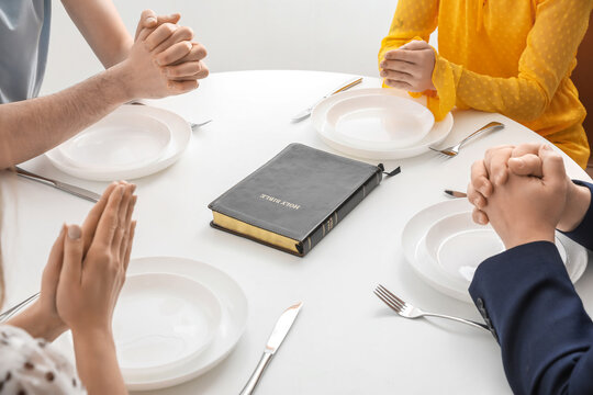 Group of people praying with Holy Bible before dinner in room, closeup