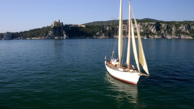 aerial drone shot of sailing boat in trieste gulf with duino castle