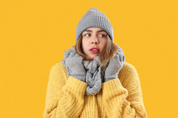 Frozen young woman in winter clothes on yellow background