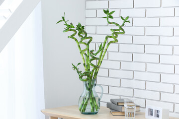 Vase with bamboo branches, books, glass of water and calendar on table near light brick wall