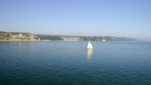 aerial drone shot of sailing boat in trieste gulf with duino castle