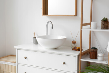 Ceramic sink and bath accessories on drawers in light bathroom