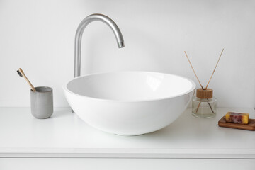 Ceramic sink and bath accessories on table in light bathroom