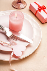 Table setting for Valentine's Day with candle and gift on beige background