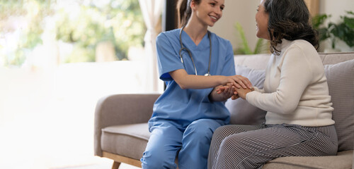 Happy patient is holding caregiver for a hand while spending time together. Elderly woman in nursing home and nurse.