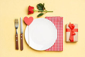 Table setting for Valentine's Day with gift and rose on yellow background