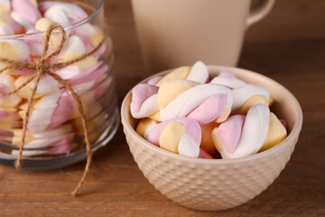 Bowl and jar of delicious twisted marshmallows on brown wooden table