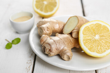 Plate with fresh ginger roots, powder and lemon on wooden table, closeup