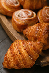 Board with delicious croissants and cinnamon rolls on black wooden background, closeup