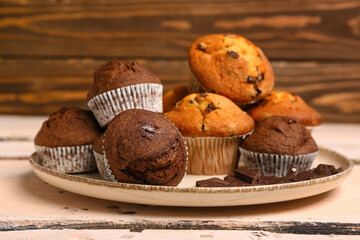 Plate with different muffins and chocolate on white wooden table